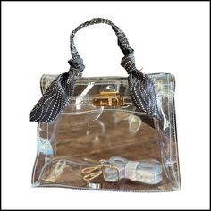 This sophisticated bag gives a nod to the iconic Kelly bag. Available with several different gameday colored twillies, the Andrea Bag measures 9.5 inches x 7 inches 4 inches. Gold hardware come with a clear cross body strap. Trendy Top Handle Bag With Clear Strap, Trendy Bags With Clear Strap And Top Handle, Trendy Top Handle Shoulder Bag With Clear Strap, Clear Crossbody Satchel With Clear Strap, Daily Use Top Handle Shoulder Bag With Clear Strap, Clear Top Handle Shoulder Bag For Everyday Use, Trendy Crossbody Satchel With Clear Strap, Trendy Clear Bags For On-the-go, Chic Rectangular Satchel With Clear Strap