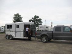 a man standing in the doorway of a horse trailer next to a gray pickup truck