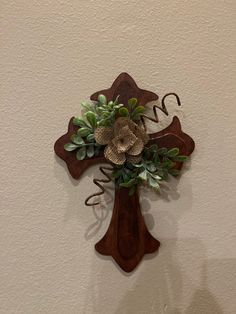 a wooden cross with flowers on it hanging from the wall in front of a white wall