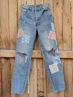 an old pair of jeans with patchwork on them hanging from a wooden fence outside