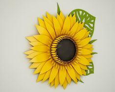 a paper sunflower with green leaves on the top and bottom, sitting on a white surface