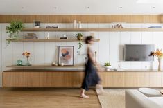 a woman walking through a living room next to a tv on a wooden entertainment center