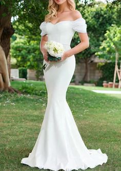 a woman in a white wedding dress standing on the grass with her hand on her hip