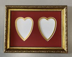 two hearts cut out of paper in a gold frame on a red wall with white background