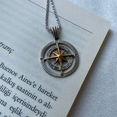 a silver and gold compass necklace on top of an open book with the text below it