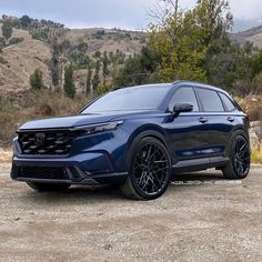 the front end of a blue suv parked on top of a dirt road near mountains