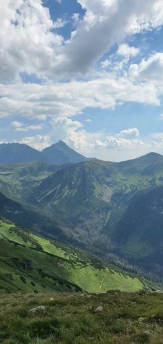 a view of mountains and valleys from the top of a hill with grass on both sides