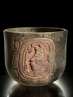 an old metal bowl with writing on the side and a face carved into it's sides