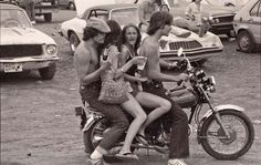 three people sitting on a motorcycle in the dirt