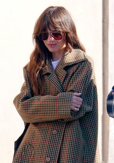 a woman with her arms crossed is wearing a plaid coat and sunglasses while standing in front of a building