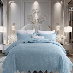 a bed with blue comforter and pillows in a room that looks like it has white flowers on the headboard