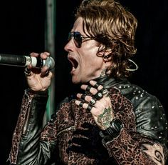 a man with long hair holding a microphone in his hand and wearing leopard print shirt