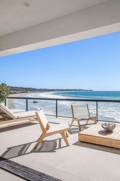 an ocean view from the balcony of a beachfront home with lounge chairs and coffee table