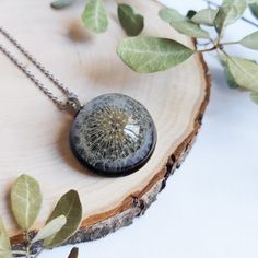 a dandelion necklace is sitting on top of a piece of wood with leaves around it