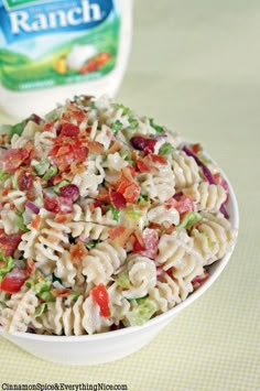 a pasta salad with bacon, lettuce and tomatoes in a white bowl on a green tablecloth