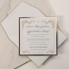 an elegant wedding card with gold foil on the front and white envelope, sitting on top of a marble surface