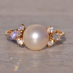 a pearl and diamond ring sitting on top of a wooden table