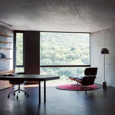 a room with a table, chair and book shelf on the floor next to a large window