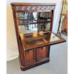 an old fashioned wooden display case with glass doors and carvings on the front, sitting on carpeted flooring