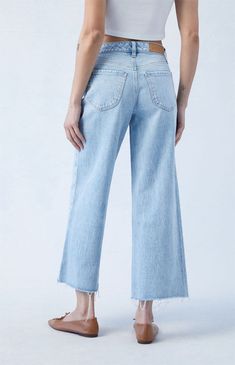 a woman wearing high rise jeans and a cropped tank top, standing in front of a white background