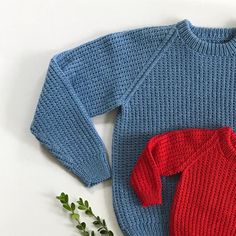 a knitted sweater with a red and blue one - piece on it next to a green plant