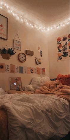 an unmade bed in a bedroom with lights strung from the ceiling and pictures on the wall