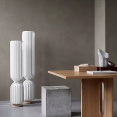 two white vases sitting on top of a wooden table next to a book shelf