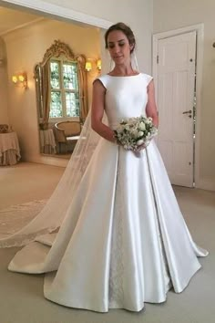 a woman in a white wedding dress standing next to a mirror and holding a bouquet