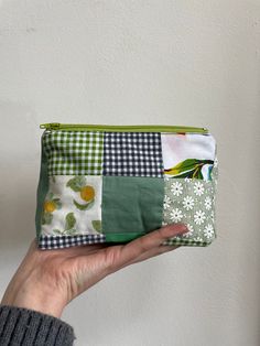 a hand holding a green and white patchwork purse