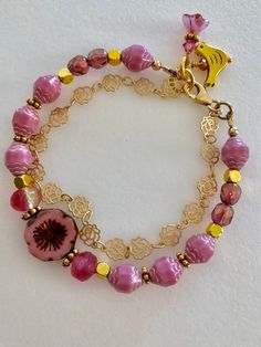 Lovely double strand beaded Premium Czech glass flower bracelet featuring Picasso pink turbine beads, Czech pink sea glass, pink cherub fire polished crystals, and single 15 mm pink Picasso pansy flower. All accented with antique gold plated daisies and shiny cubes. Satin Hamilton rose chain adds the perfect delicate second strand. Premium gold electroplated brass chain in satin finish with intricate rose flower pattern. Bracelet is beaded on professional Soft Flex beading wire with high quality Adjustable Pink Bracelets, Pink Single Strand Beaded Bracelet As Gift, Double Strand Faceted Beads Bracelet For Gift, Pink Single Strand Beaded Bracelet For Gift, Faceted Beads Double Strand Bracelet As Gift, Colorful Beads Double Strand Bracelet As Gift, Pink Glass Beaded Bracelets, Pink Single Strand Beaded Bracelet Gift, Adjustable Pink Single Strand Beaded Bracelets