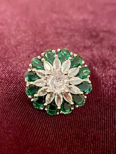 a green and white brooch sitting on top of a red velvet covered tablecloth