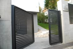 two black gates are open on the side of a concrete building with grass and trees in the background