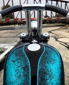 the handlebars of a blue motorcycle parked in front of a bridge