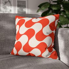 an orange and white pillow sitting on top of a gray couch next to a plant