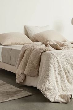 an unmade bed with beige linens and pillows on it in a white room