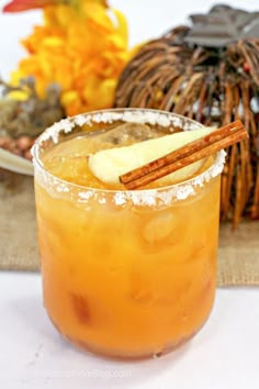 a drink with an apple and cinnamon garnish on the rim, sitting next to a decorative pumpkin