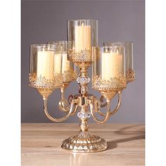 a gold candelabra with five candles on it and some clear glasses in the middle