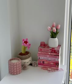 a white table topped with pink books and vases filled with flowers next to each other