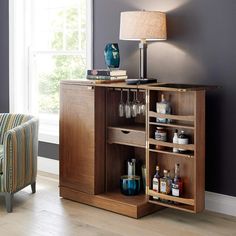 a wooden cabinet with wine glasses and bottles on the bottom shelf next to a lamp