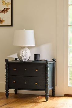 a black dresser with two drawers and a white lamp on top of it next to a window