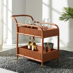 a wooden bar cart with wine glasses and bottles on it in front of a potted plant