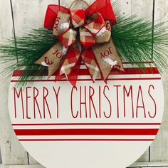 a merry christmas sign hanging on the side of a wooden wall with a bow and evergreen