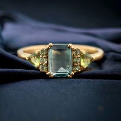 an emerald and yellow sapphire ring sitting on top of a black cloth