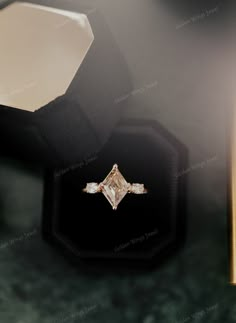 an engagement ring sitting on top of a black velvet box next to a golden stick