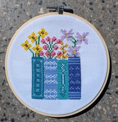 a cross stitched picture of two blue vases with flowers in them on the ground