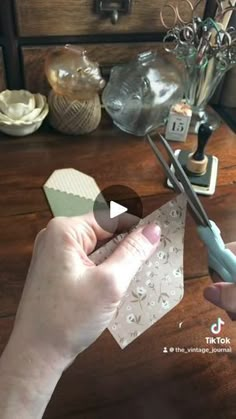 a person is cutting paper with scissors on a wooden table in front of a vase