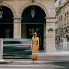 a woman standing on the street in front of an old building with cars passing by