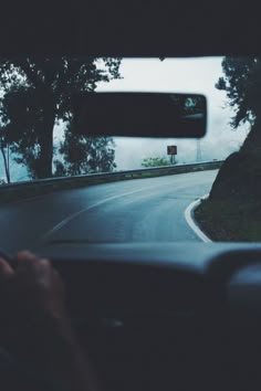 a person is driving down the road with their hand on the steering wheel, and there are trees in the background