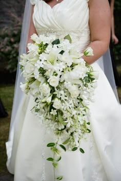 a woman in a wedding dress holding a bridal bouquet with white flowers and greenery