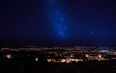 the night sky is filled with stars and bright lights, as seen from an overlook